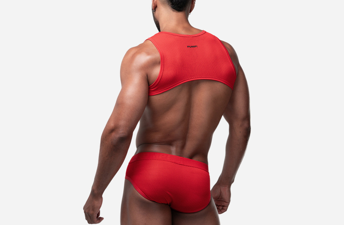 A muscular man shown from behind wearing a red athletic tank top and matching red briefs against a light gray studio background.